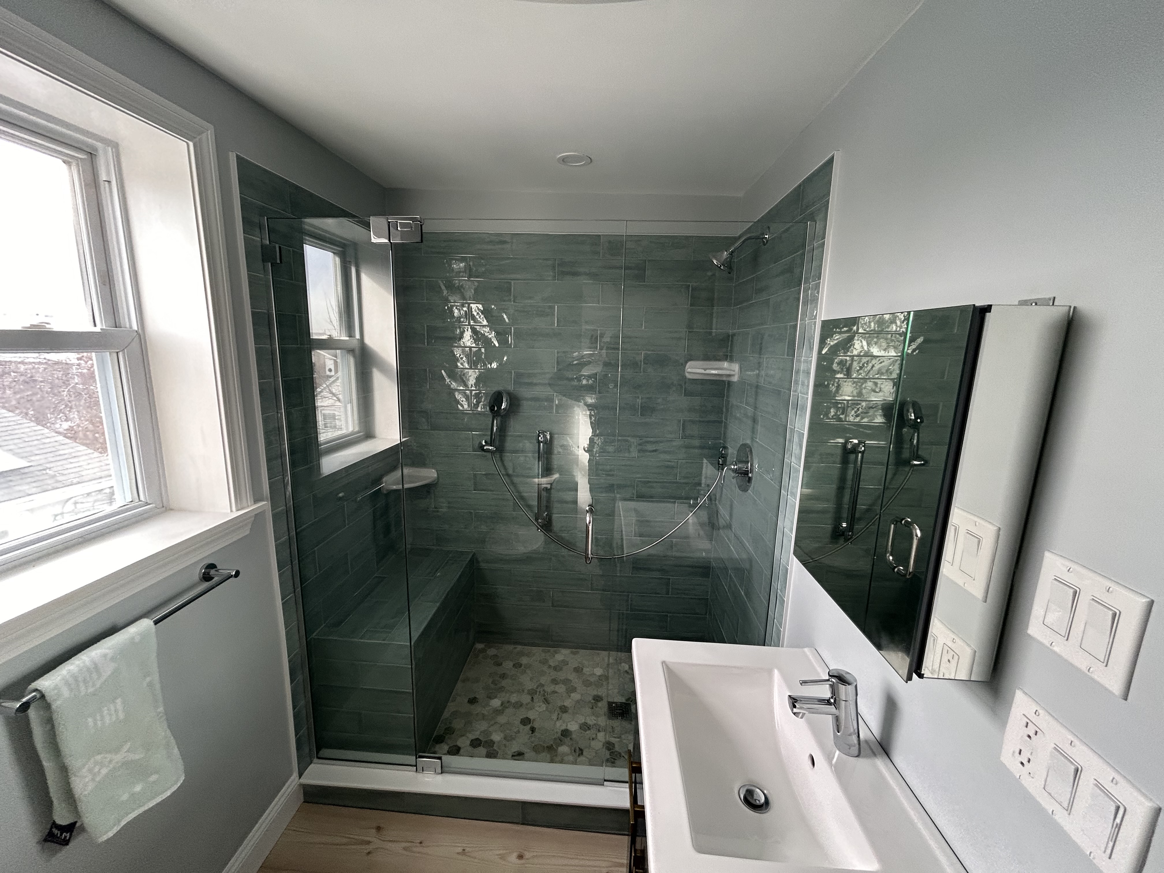 Walk-in shower with slate green subway tile, frameless glass enclosure, and built-in bench by Bulldog Construction