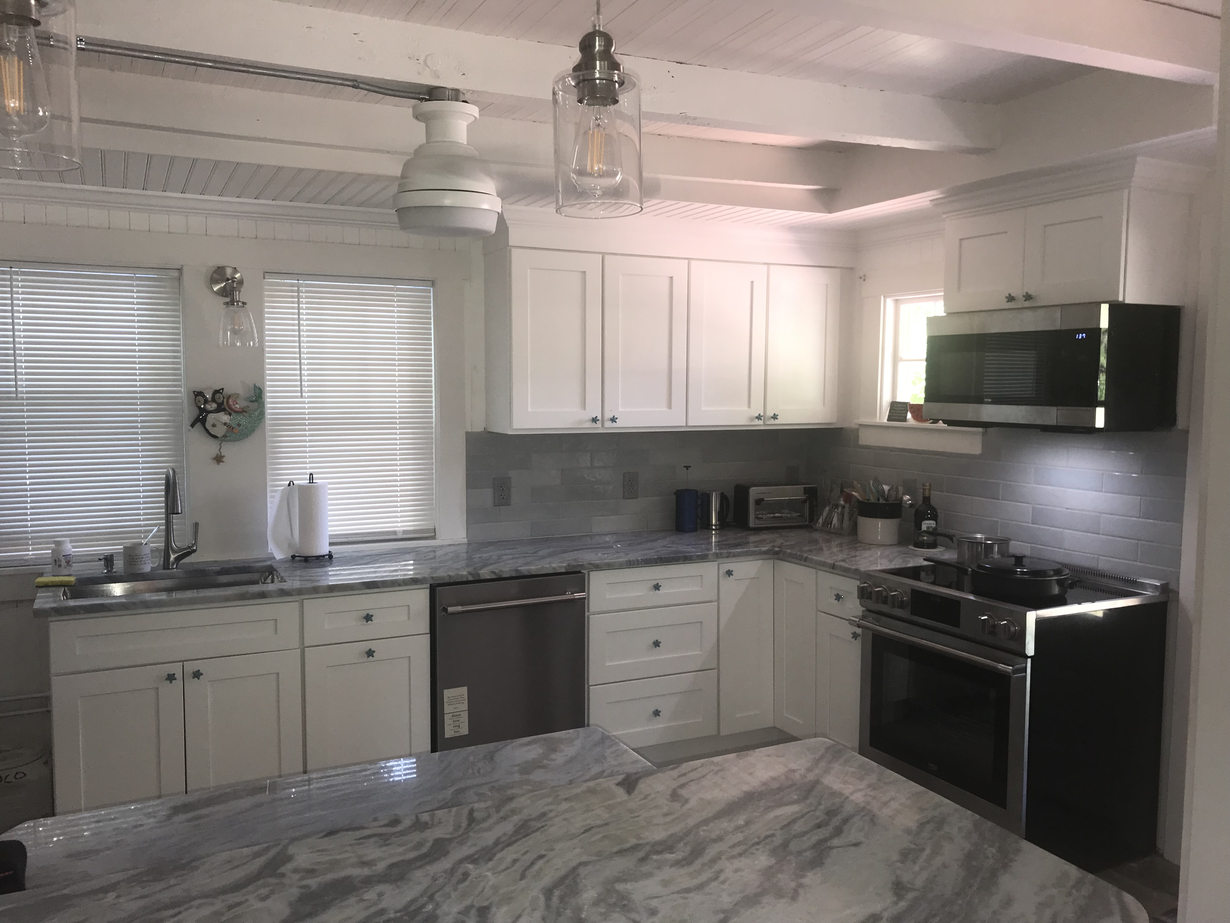 Bright renovated white kitchen with new appliances, light floors, and white brick accent column by Bulldog Construction