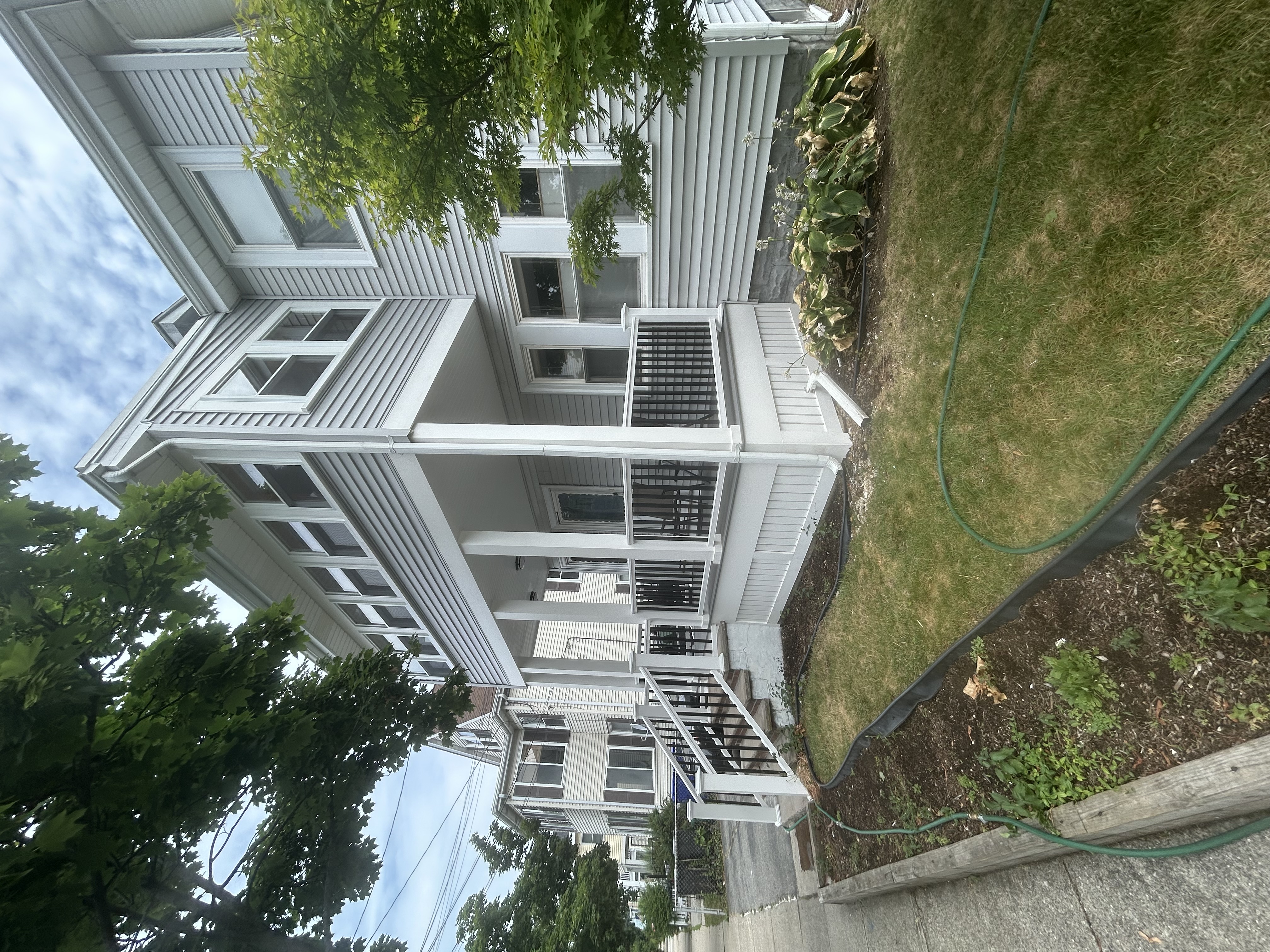 Completed two-story porch with light grey siding, white columns, and black balusters after the porch build by Bulldog Construction